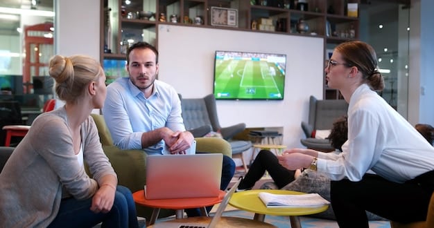 A medium shot of a group of sports managers in a meeting room, discussing strategies and looking at a projected graph on the wall. The atmosphere is professional and collaborative, with laptops and documents spread across the table.