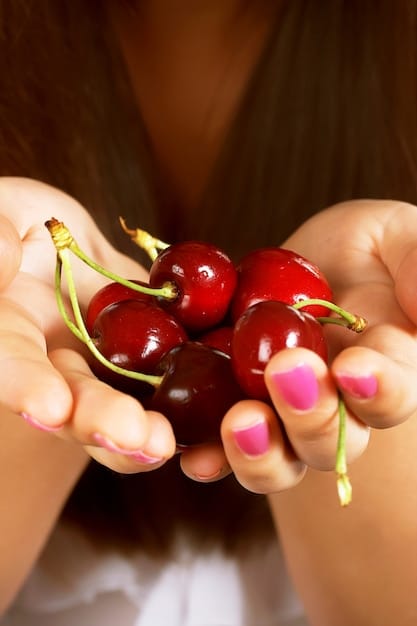 A close-up shot of a handful of bright red acerola cherries, showcasing their vibrant color and small size. Some of the cherries are cut in half, revealing the juicy pulp and small seeds inside. The background is a blurred green, suggesting the acerola is fresh from the tree.