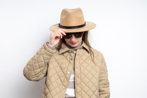 A medium shot of a person wearing a wide-brimmed hat, sunglasses, and a light-colored long-sleeved shirt, standing on a sunny beach with palm trees in the background. The focus is on the protective clothing and accessories.