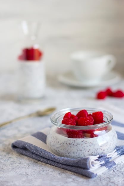 A creamy chocolate avocado mousse in a clear glass bowl, topped with fresh raspberries and a sprinkle of chia seeds, presented on a modern countertop with soft natural light.