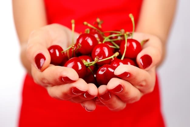 A close-up shot of a handful of bright red acerola cherries, held in a woman's hand. The background is a blurred image of an acerola tree with lush green leaves. The lighting is soft and natural, highlighting the vibrant color and texture of the fruit.